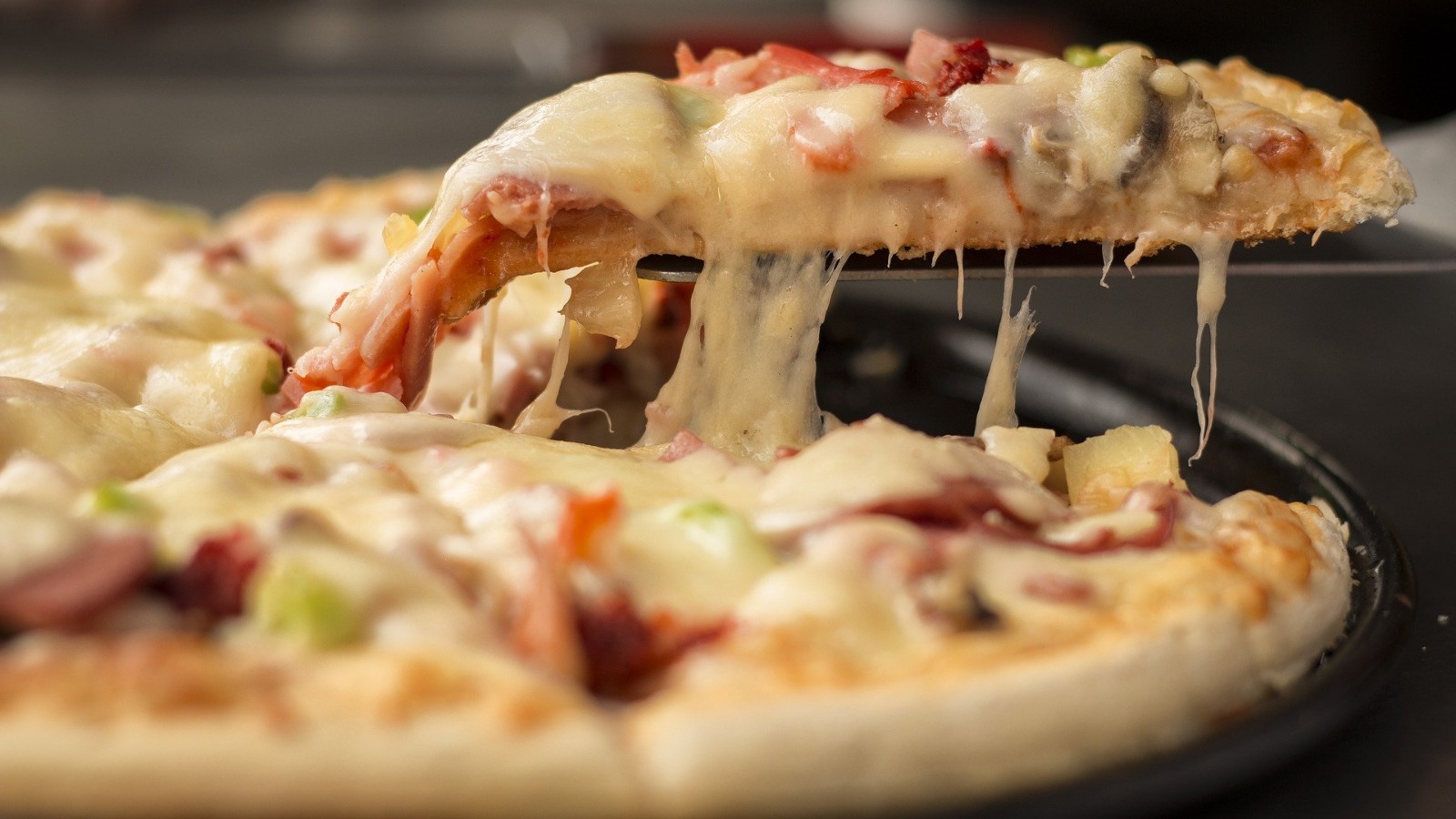 Porción de pizza con queso fundido, jamón y champiñones